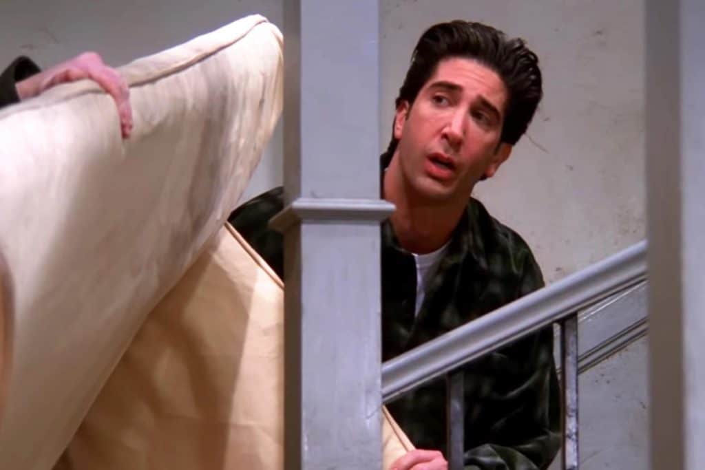 A still of Ross from Friends trying to direct a couch up the stairs.